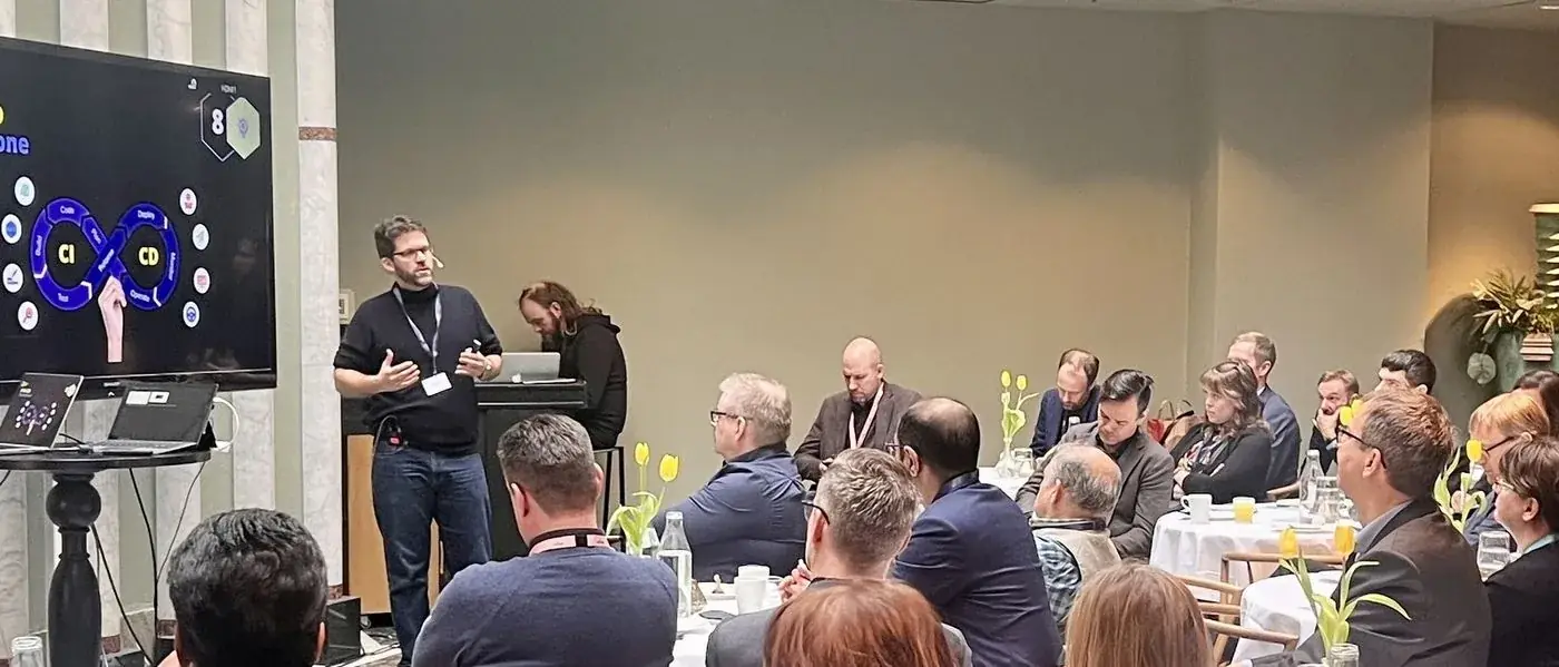 Mario A. Brückner spricht vor einem voll besetzten Konferenzsaal an runden Tischen